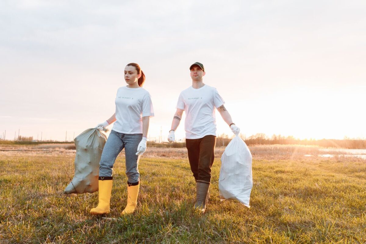 À propos Two volunteers cleaning a field by picking up trash in sacks during sunset.